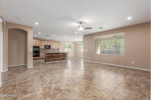 kitchen featuring light brown cabinetry, black appliances, a kitchen island with sink, ceiling fan with notable chandelier, and backsplash