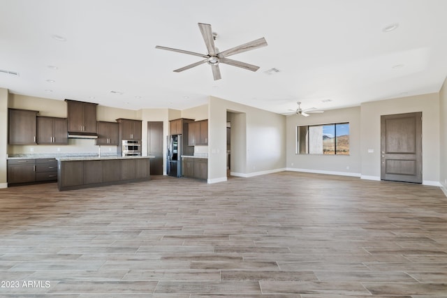 kitchen with dark brown cabinets, an island with sink, ceiling fan, appliances with stainless steel finishes, and light hardwood / wood-style floors