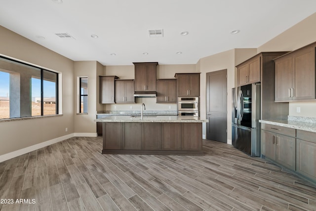 kitchen featuring light stone countertops, stainless steel appliances, sink, and light hardwood / wood-style flooring