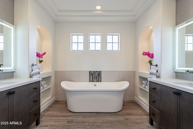 bathroom with wood-type flooring, tile walls, a bathtub, vanity, and a tray ceiling