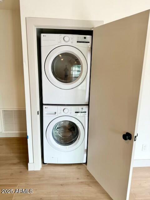 clothes washing area featuring laundry area, visible vents, stacked washer / drying machine, and light wood finished floors