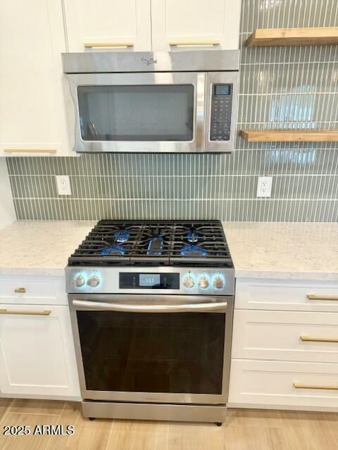 kitchen featuring light stone countertops, tasteful backsplash, appliances with stainless steel finishes, and white cabinetry