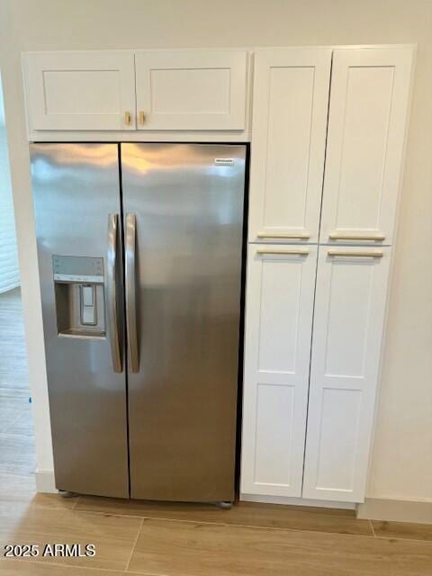 kitchen with wood finish floors, baseboards, stainless steel fridge with ice dispenser, and white cabinetry