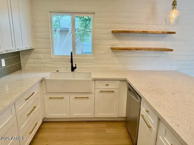 kitchen with a sink, light wood-type flooring, decorative backsplash, white cabinetry, and stainless steel dishwasher