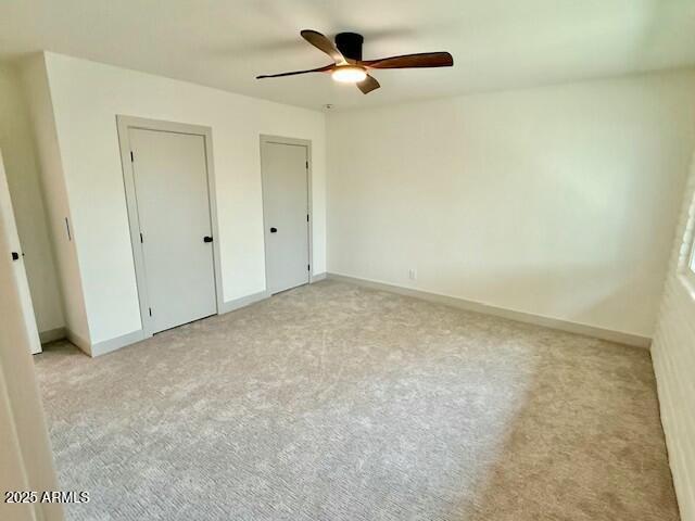 unfurnished bedroom with a ceiling fan, baseboards, two closets, and light carpet