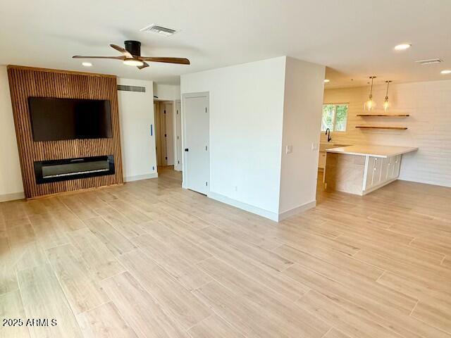 unfurnished living room featuring baseboards, a ceiling fan, visible vents, and light wood-type flooring