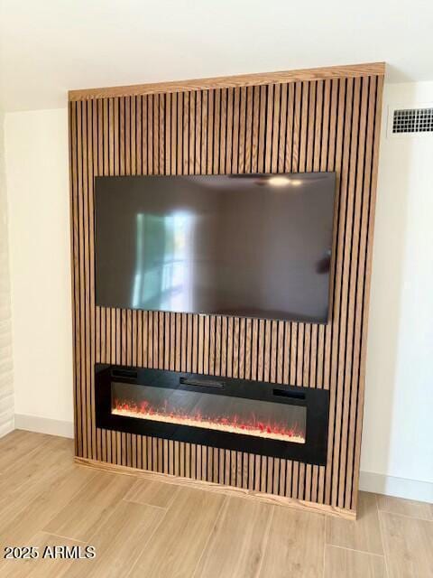 room details featuring baseboards, wood finished floors, visible vents, and a glass covered fireplace