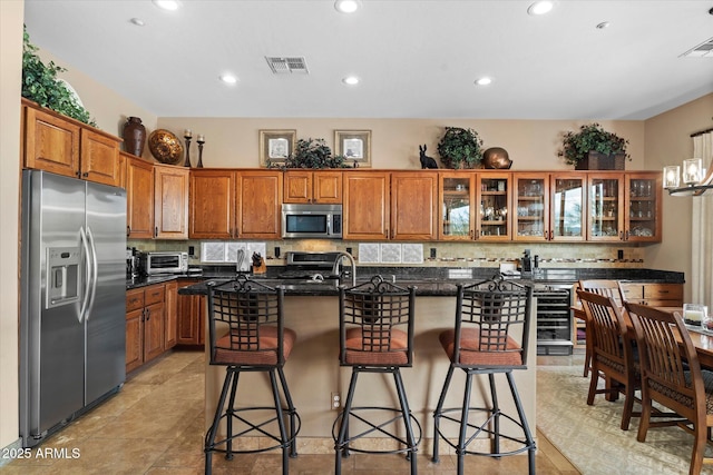 kitchen with a kitchen breakfast bar, appliances with stainless steel finishes, backsplash, and a center island with sink