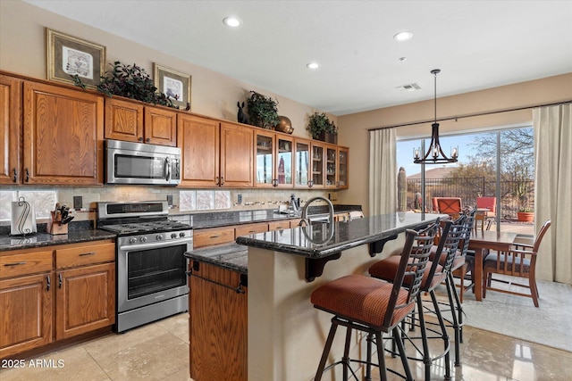 kitchen with decorative light fixtures, backsplash, an island with sink, a kitchen breakfast bar, and stainless steel appliances