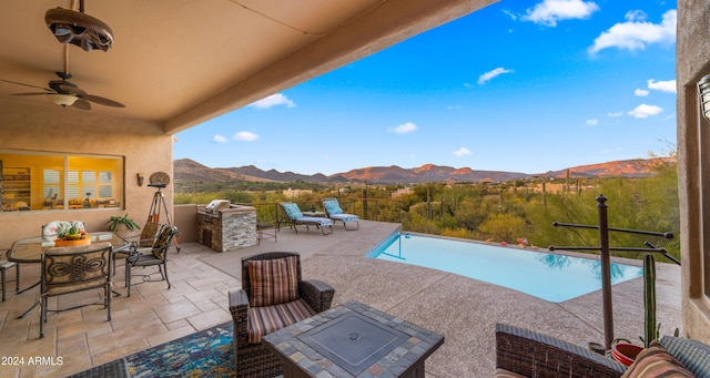 view of swimming pool with a patio area, a mountain view, ceiling fan, and exterior kitchen