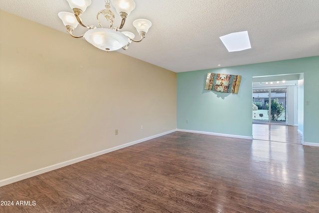 empty room featuring a textured ceiling, dark hardwood / wood-style floors, a skylight, and a chandelier