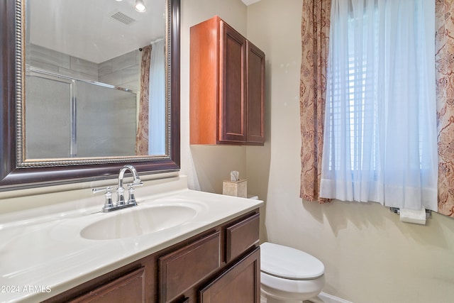 bathroom featuring toilet, vanity, and a shower with door