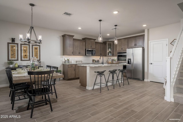 kitchen featuring stainless steel appliances, light stone countertops, hanging light fixtures, and a center island with sink