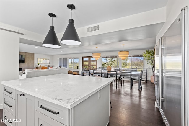 kitchen featuring high end fridge, dark hardwood / wood-style floors, a kitchen island, hanging light fixtures, and light stone countertops