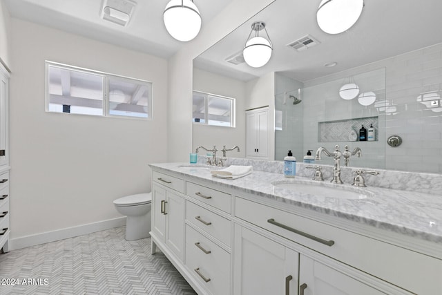 bathroom with tile floors, dual bowl vanity, a tile shower, and toilet