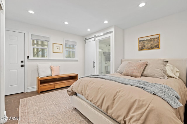 bedroom with wood-type flooring, connected bathroom, and a barn door