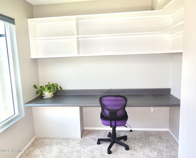 unfurnished office featuring carpet floors, baseboards, and built in desk