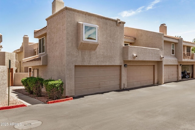 view of front of house with stucco siding, a chimney, a tile roof, and a garage