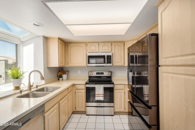 kitchen featuring light countertops, appliances with stainless steel finishes, a sink, and light brown cabinets