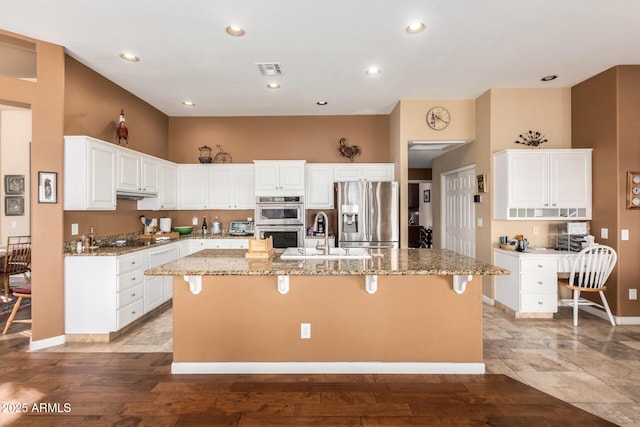 kitchen with stainless steel appliances, a kitchen island with sink, white cabinets, light stone counters, and sink