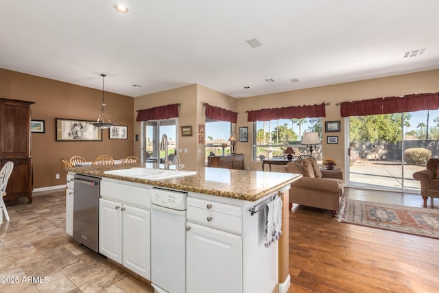 kitchen with decorative light fixtures, sink, white cabinets, and an island with sink