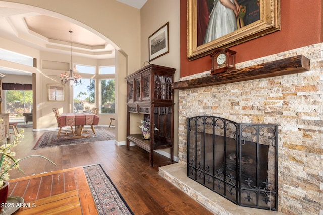 interior space featuring a high ceiling, dark wood-type flooring, a stone fireplace, an inviting chandelier, and a tray ceiling