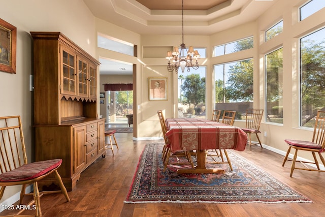 dining space featuring dark hardwood / wood-style floors, a raised ceiling, a towering ceiling, and an inviting chandelier