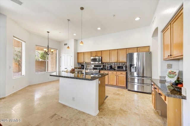 kitchen featuring appliances with stainless steel finishes, dark stone countertops, backsplash, and an island with sink