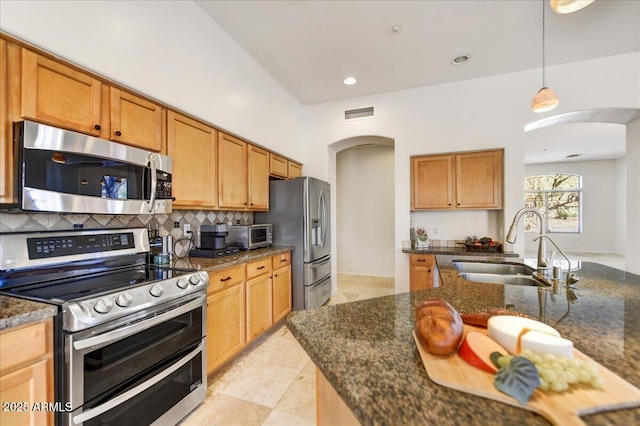 kitchen featuring arched walkways, pendant lighting, tasteful backsplash, appliances with stainless steel finishes, and a sink