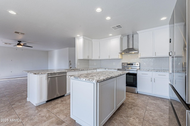 kitchen with white cabinetry, wall chimney exhaust hood, appliances with stainless steel finishes, a kitchen island, and kitchen peninsula