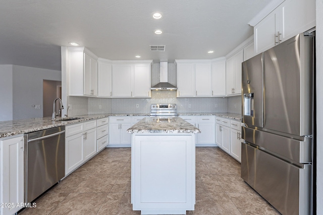 kitchen featuring light stone countertops, wall chimney range hood, a kitchen island, white cabinets, and appliances with stainless steel finishes