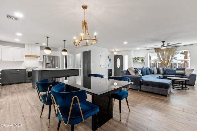 dining room with ceiling fan with notable chandelier and light hardwood / wood-style flooring