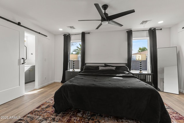 bedroom featuring ensuite bathroom, ceiling fan, a barn door, light wood-type flooring, and multiple windows