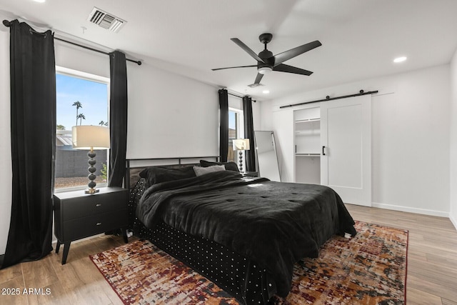 bedroom with a barn door, a spacious closet, light hardwood / wood-style flooring, and ceiling fan