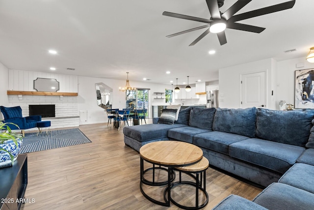 living room with hardwood / wood-style floors, ceiling fan with notable chandelier, and a brick fireplace