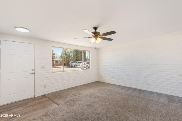 carpeted entryway featuring brick wall, a ceiling fan, and wood finished floors