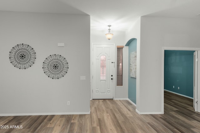 entrance foyer featuring arched walkways, wood finished floors, and baseboards