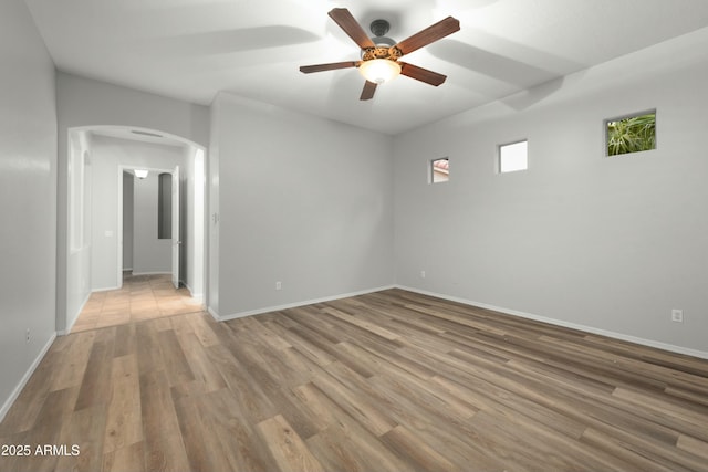 unfurnished room featuring arched walkways, ceiling fan, baseboards, and wood finished floors