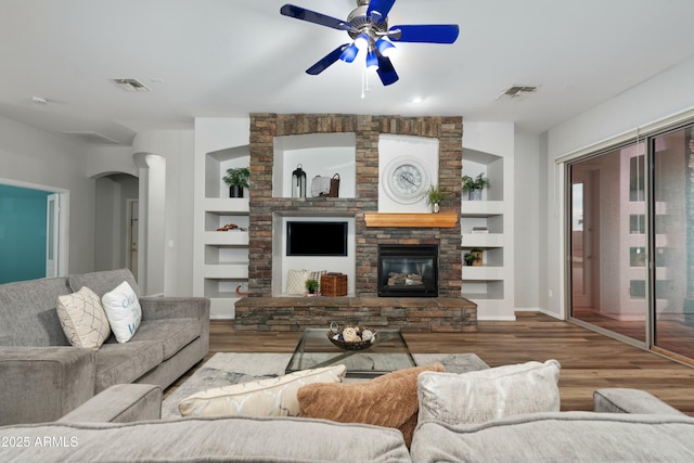 living room featuring a stone fireplace, wood finished floors, visible vents, and built in features