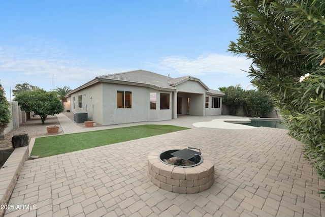 back of property with stucco siding, central AC unit, an outdoor fire pit, a patio area, and a fenced backyard