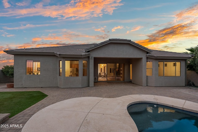 rear view of property with a patio, an attached garage, a tile roof, an outdoor pool, and stucco siding