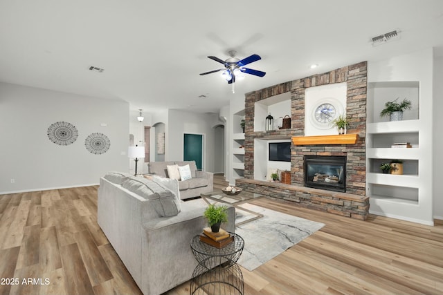 living area featuring arched walkways, ceiling fan, wood finished floors, built in shelves, and a fireplace