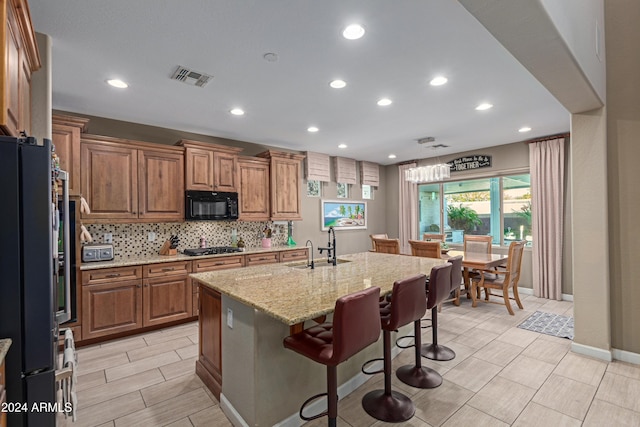 kitchen with sink, light stone counters, a breakfast bar area, a center island with sink, and black appliances