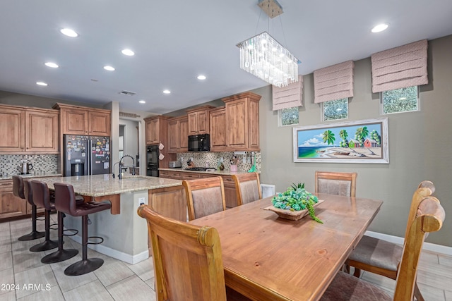 kitchen with tasteful backsplash, light stone counters, a notable chandelier, a kitchen island with sink, and black appliances