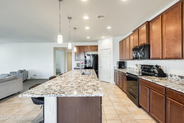 kitchen featuring pendant lighting, a kitchen island with sink, black appliances, light stone countertops, and a kitchen bar