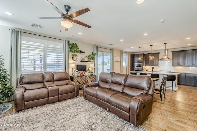 living room with ceiling fan, light wood-type flooring, sink, and a wealth of natural light