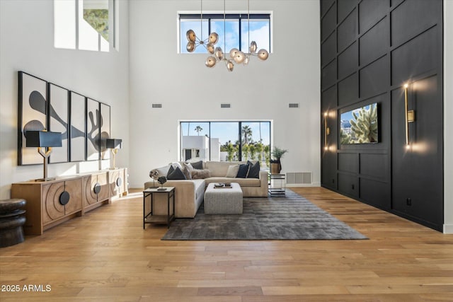 living room with a high ceiling, an inviting chandelier, and light hardwood / wood-style flooring