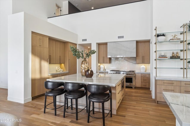 kitchen with a kitchen island with sink, wall chimney range hood, light hardwood / wood-style floors, and stainless steel stove