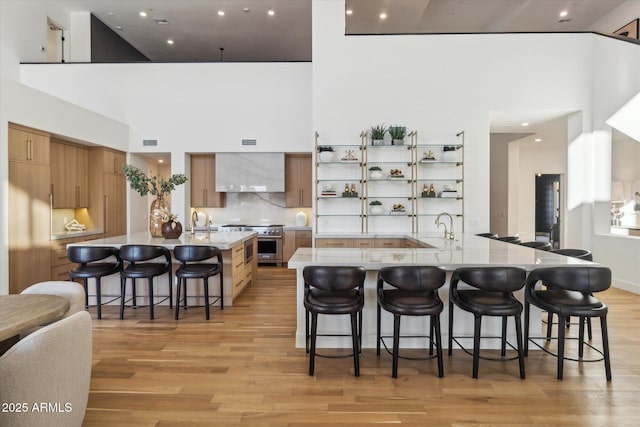 kitchen featuring wall chimney exhaust hood, high end stainless steel range oven, a high ceiling, tasteful backsplash, and a breakfast bar area