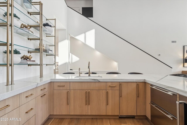 bar with sink, light hardwood / wood-style floors, light stone countertops, and light brown cabinets